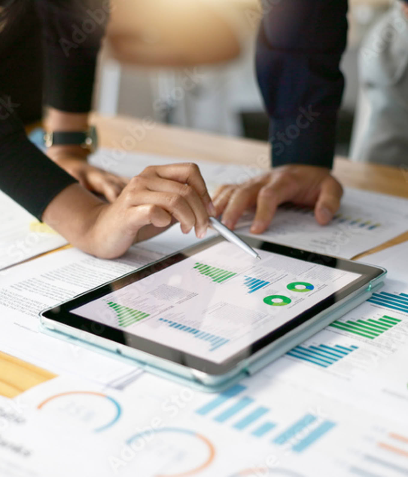 Personen arbeiten an einem Tisch mit Diagrammen und einem Tablet.